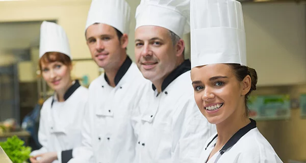 Four culinary professionals in white coats and chefs' hats stand in a line.