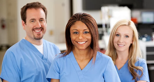 A male and two female nurses in scrubs smileing.