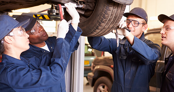 Four mechanics wear protective glasses while working on a car's tire in the workshop.