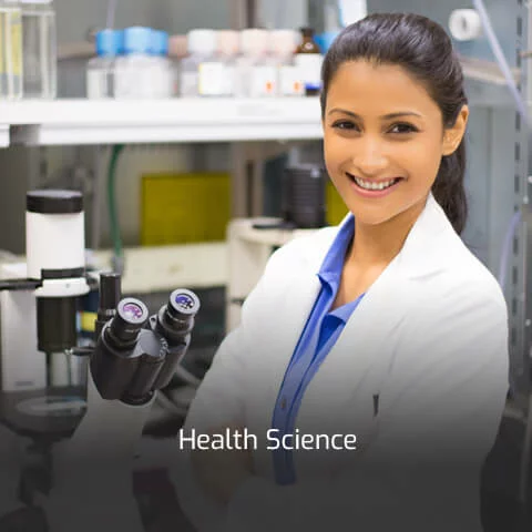 A female health science professional in a white lab coat stands next to a microscope.