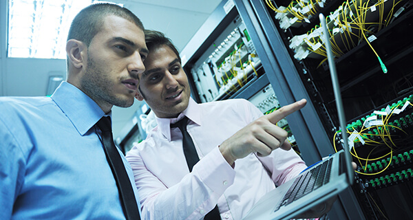 Two information technology professionals examine information on a laptop computer.